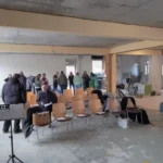 Das Bild zeigt viele Personen, die im der Baustelle einen Kaffee trinken.